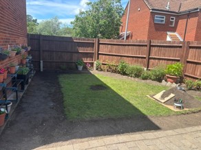 A communal garden space in sunlight with newly painted brown fences and turf.