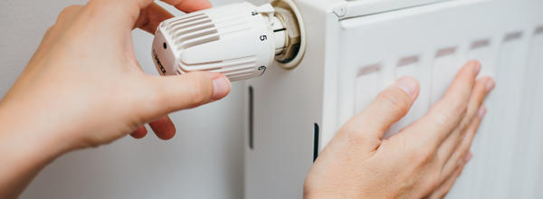A white radiator. A hand is turning the dial knob on the top of the radiator.