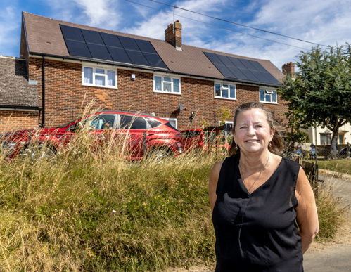 A woman is stood in front of two semi detached homes with solar panels on the roof.