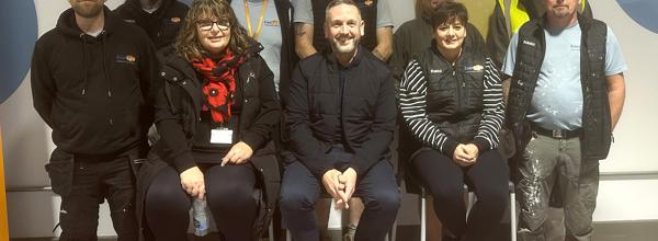 Members of Eastlight's Healthy Homes Team pictured at Eastlight's Marks Tey hub. They are gathered together in a group, with the back row of staff standing, and the front row sitting directly in front of them on stalls.