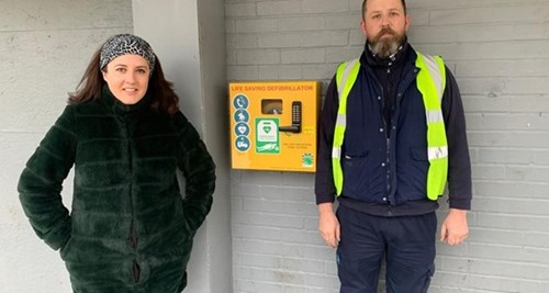 Two people standing by an installed defibrillator