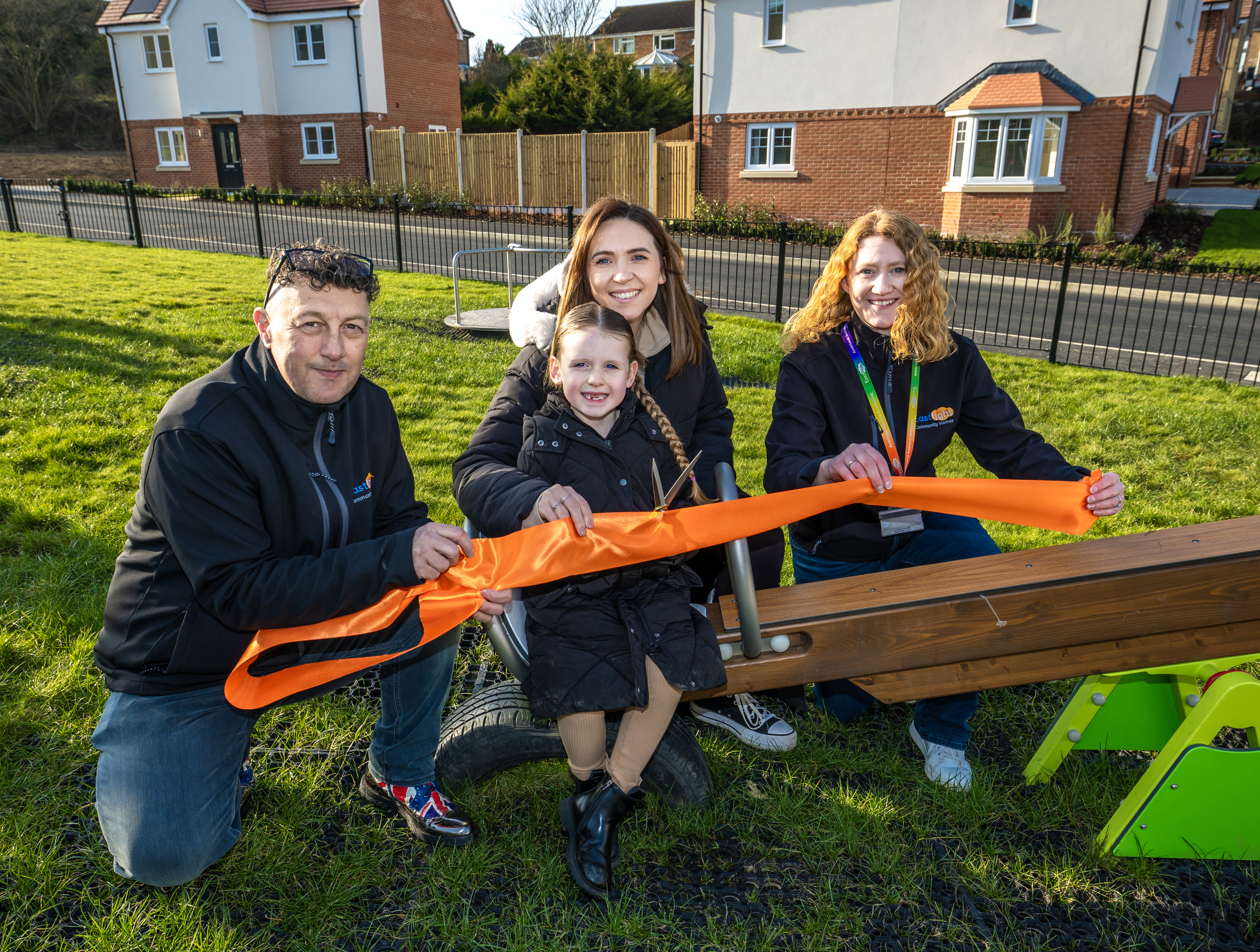 Eastlight's Debbie Mitchell and Andy Allocca are with Eastlight family Charlea and her daughter Lilly. They are all holding onto a ribbon while at an event opening the new playground.