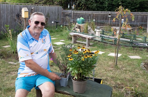 Jeff Spencer sitting on a bench in the community garden, next to two plant pots