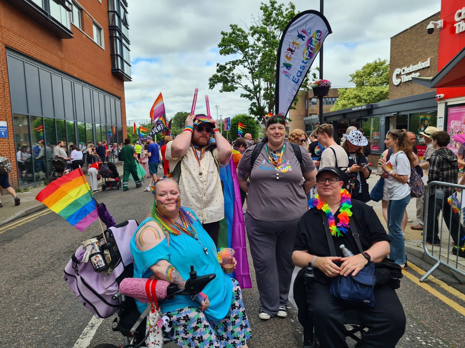 Members of EastPride, Eastlight’s LGBTQ+ resident group, pose for a photo during a Pride parade, with rainbow flags, event banners and other participants visible in the background.