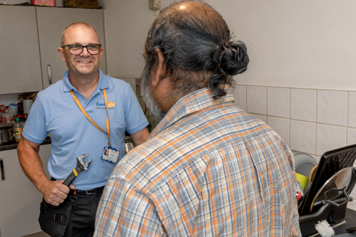 An Eastlight staff member holding a spanner and speaking to a resident in their home