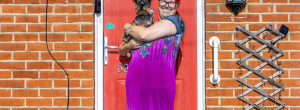 Eastlight resident in front of the door to their home, holding a dog and smiling at the camera