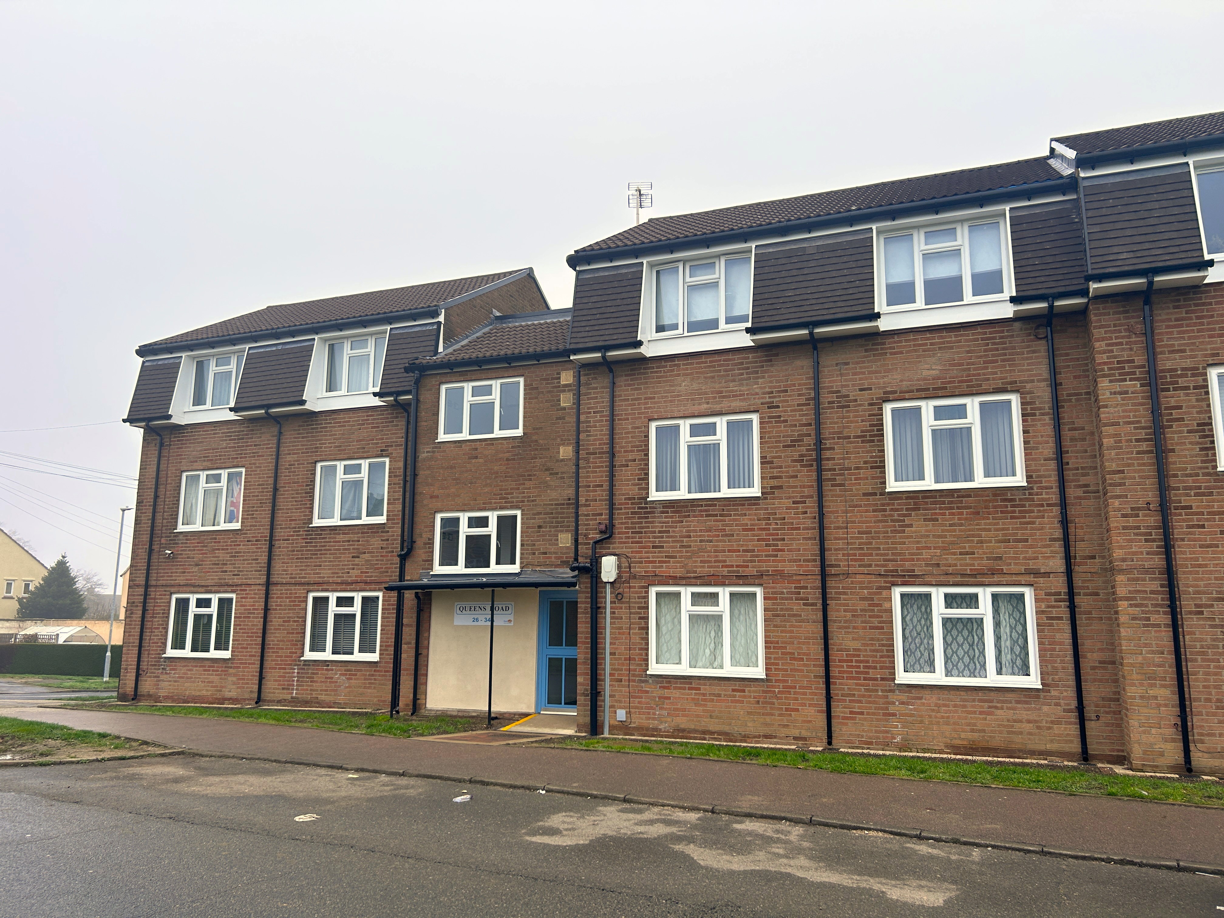 A block of three storey flats next to a road.