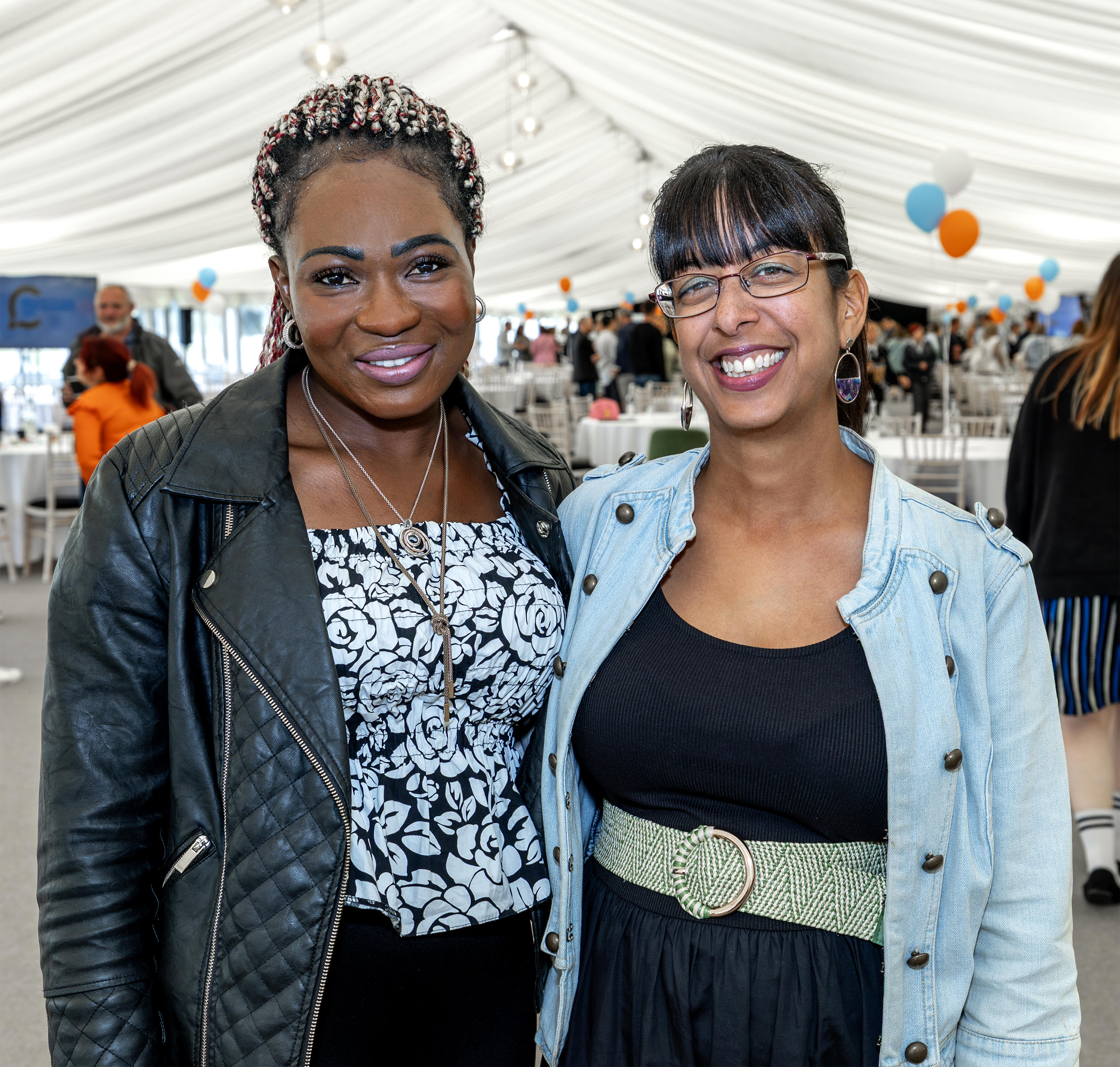 Two women are stood next to each other with their arm around each other. They are smiling.