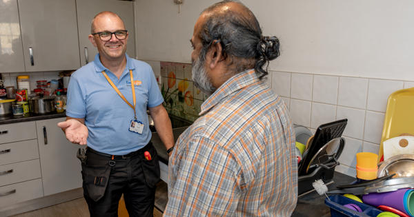 Two men are stood together. One is wearing an Eastlight blue polo shirt and the other is a resident. They are talking to each other.