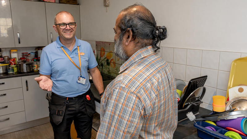 Two men are stood together. One is wearing an Eastlight blue polo shirt and the other is a resident. They are talking to each other.