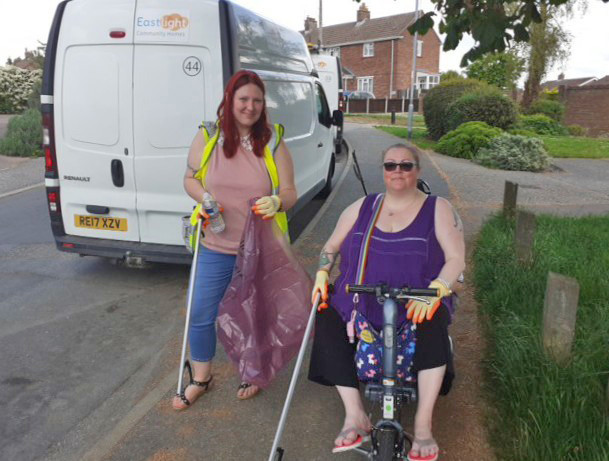 Two women standing outside on a housing estate, in front of a white van. They are both holding litter-pick sticks and bags of rubbish, smiling at the camera.