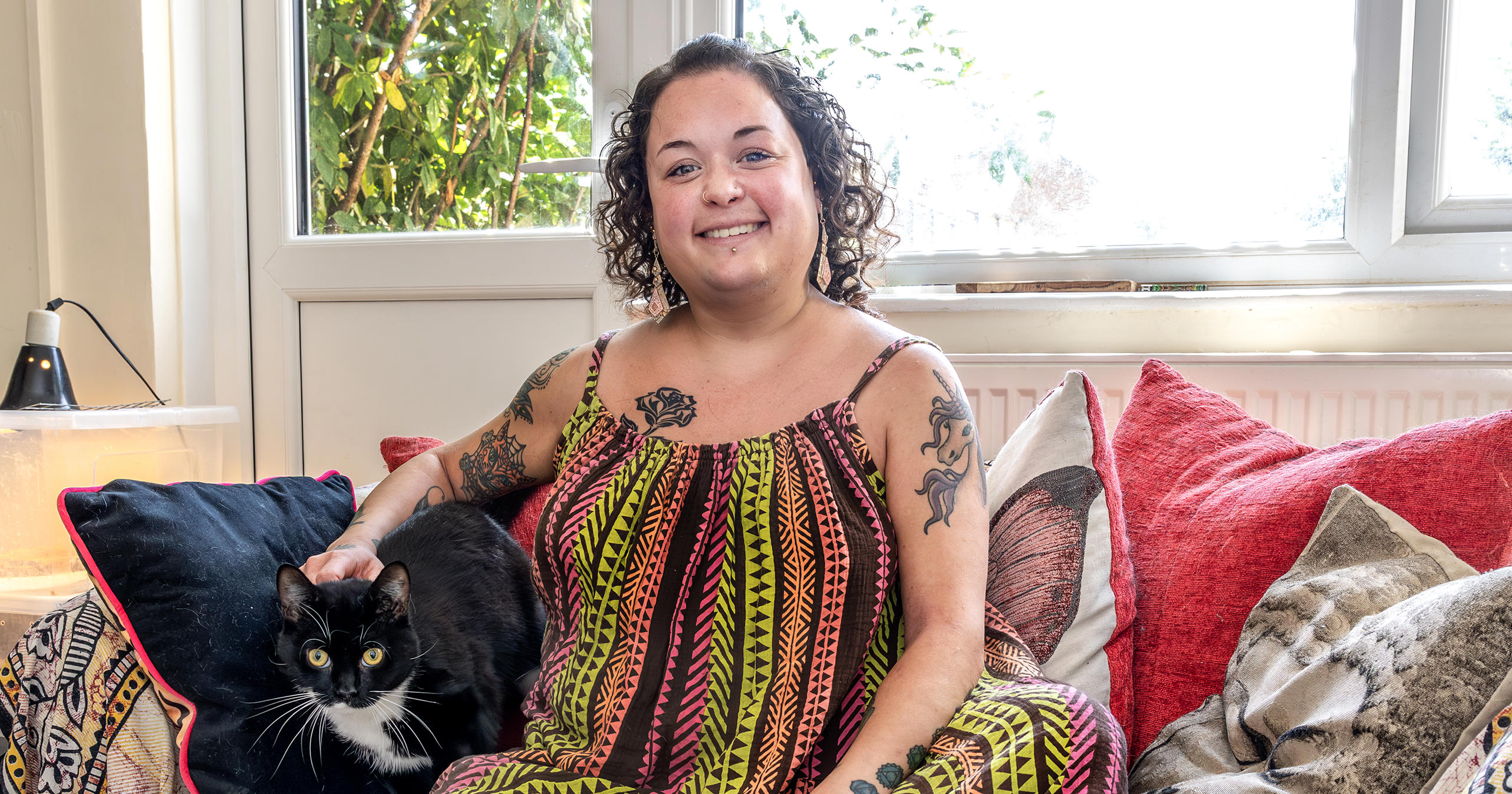 Young resident Bobbie Town is sat on a sofa in her home. Her black and white cat is sat next to her.