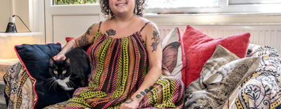 Young resident Bobbie Town is sat on a sofa in her home. Her black and white cat is sat next to her.
