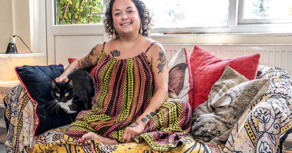 Young resident Bobbie Town is sat on a sofa in her home. Her black and white cat is sat next to her.