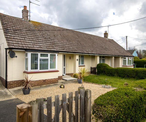 A cream coloured bungalow with white windows and red window sills.