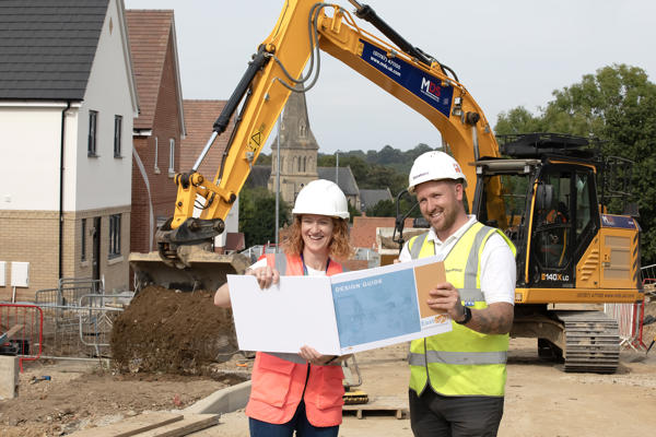 Two people on a development site holding up a large document and smiling