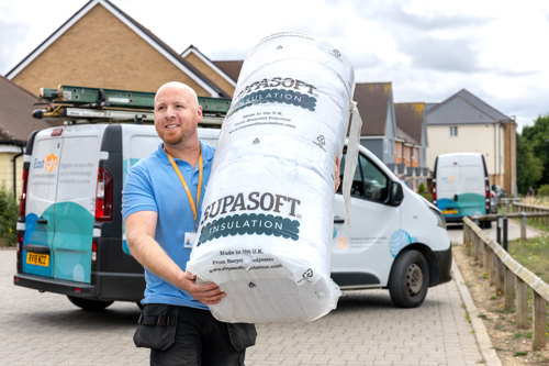 An Eastlight tradesmen is carrying a large bag of Supasoft insulation. Behind him is an Eastlight van.