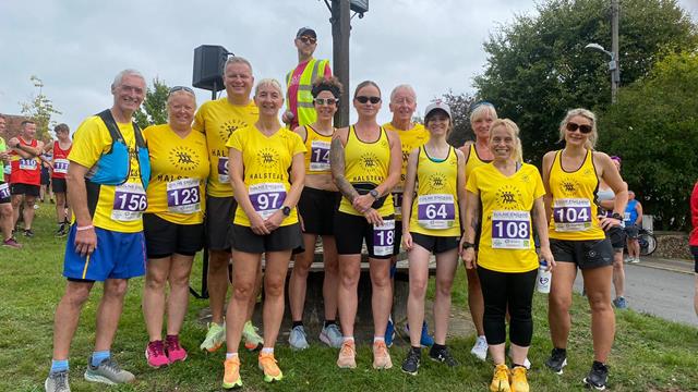 A group of Halstead Road Runners wearing yellow running jerseys. The 11 members are all smiling towards the camera.