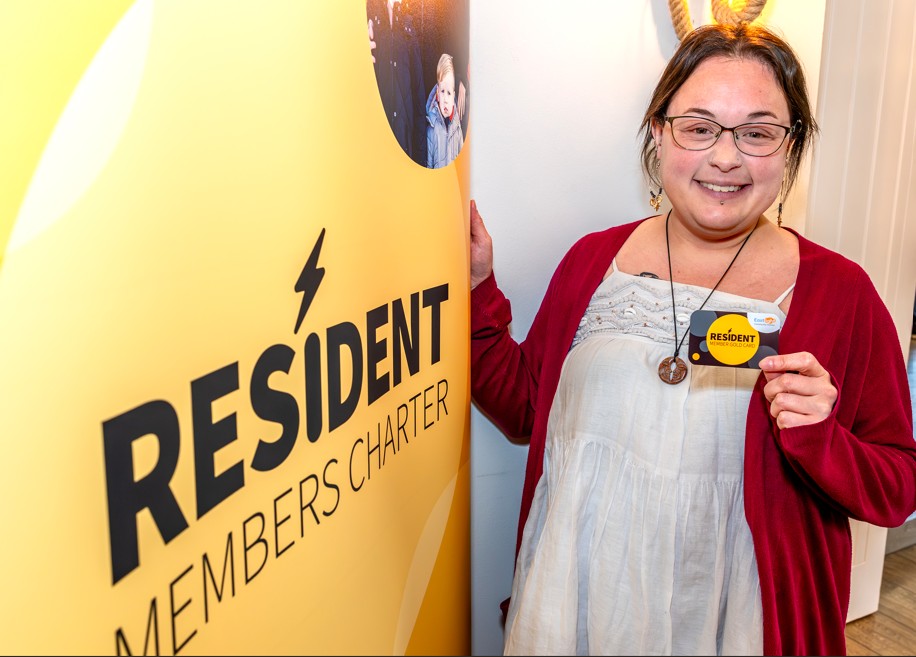 Eastlight resident, Bobbie, holding up her Gold card and standing to the right of the Resident Members Charter banner.