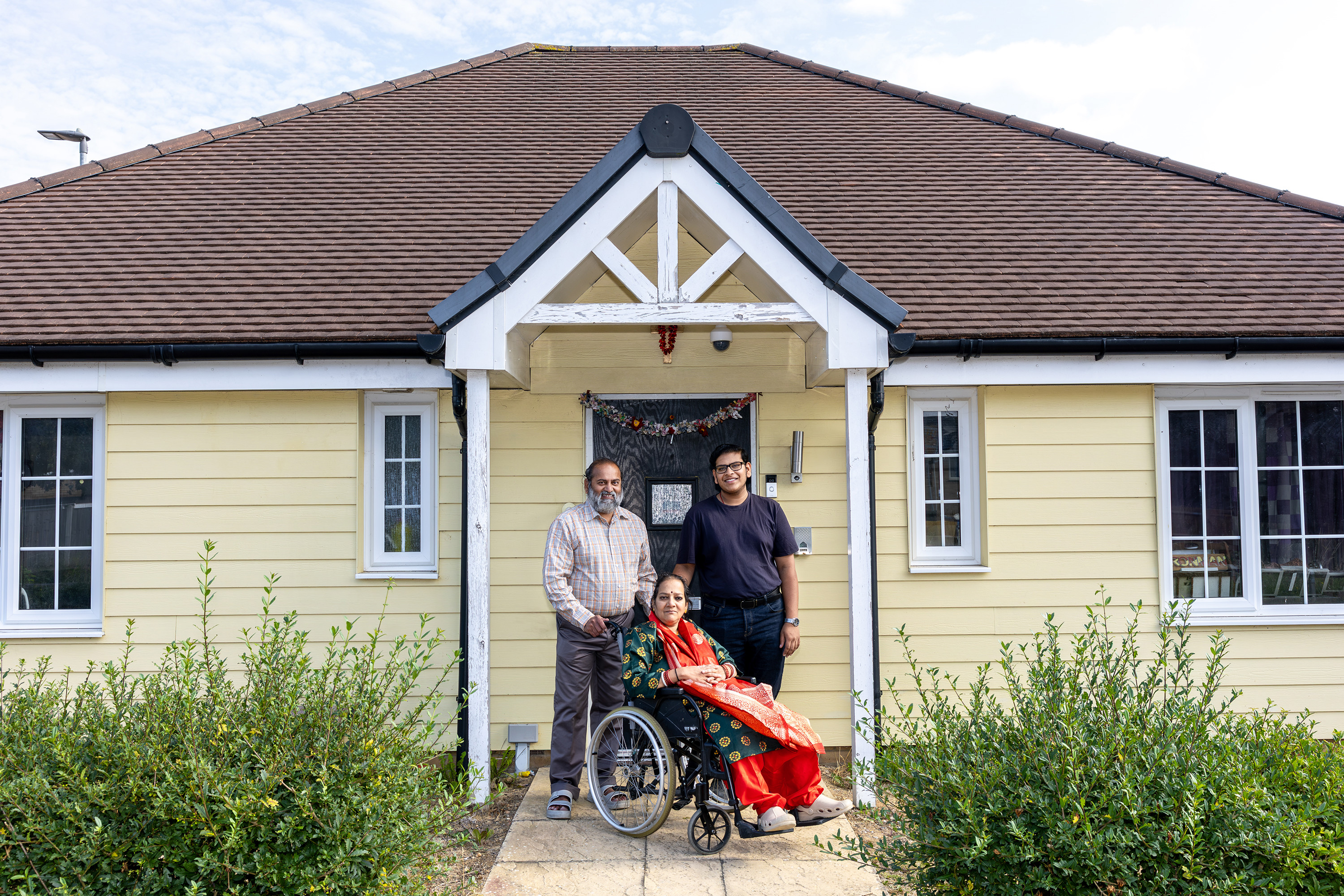 An Eastlight family are together outside the front of their home. Two men are stood behind a woman sat in a wheelchair.