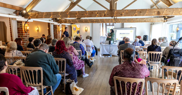 A photo from the back of the room, behind Audience members who are looking towards the stage during a presentation at the Resident Members Charter celebration event, April 2026.