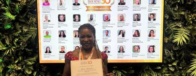 Mavis is stood in front of a screen detailing the 30 individuals featured in in Inside Housing Management 30. She is holding a certificate.