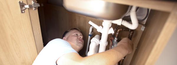A member of Eastlight’s Home Solutions Team carries out plumbing repairs beneath a kitchen sink in a resident’s home.