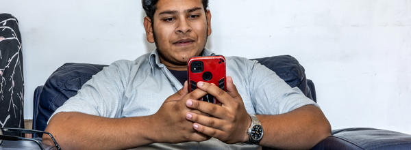 A younger Eastlight resident sitting on a black leather armchair in his home, holding onto and looking down at his mobile phone in his hands.