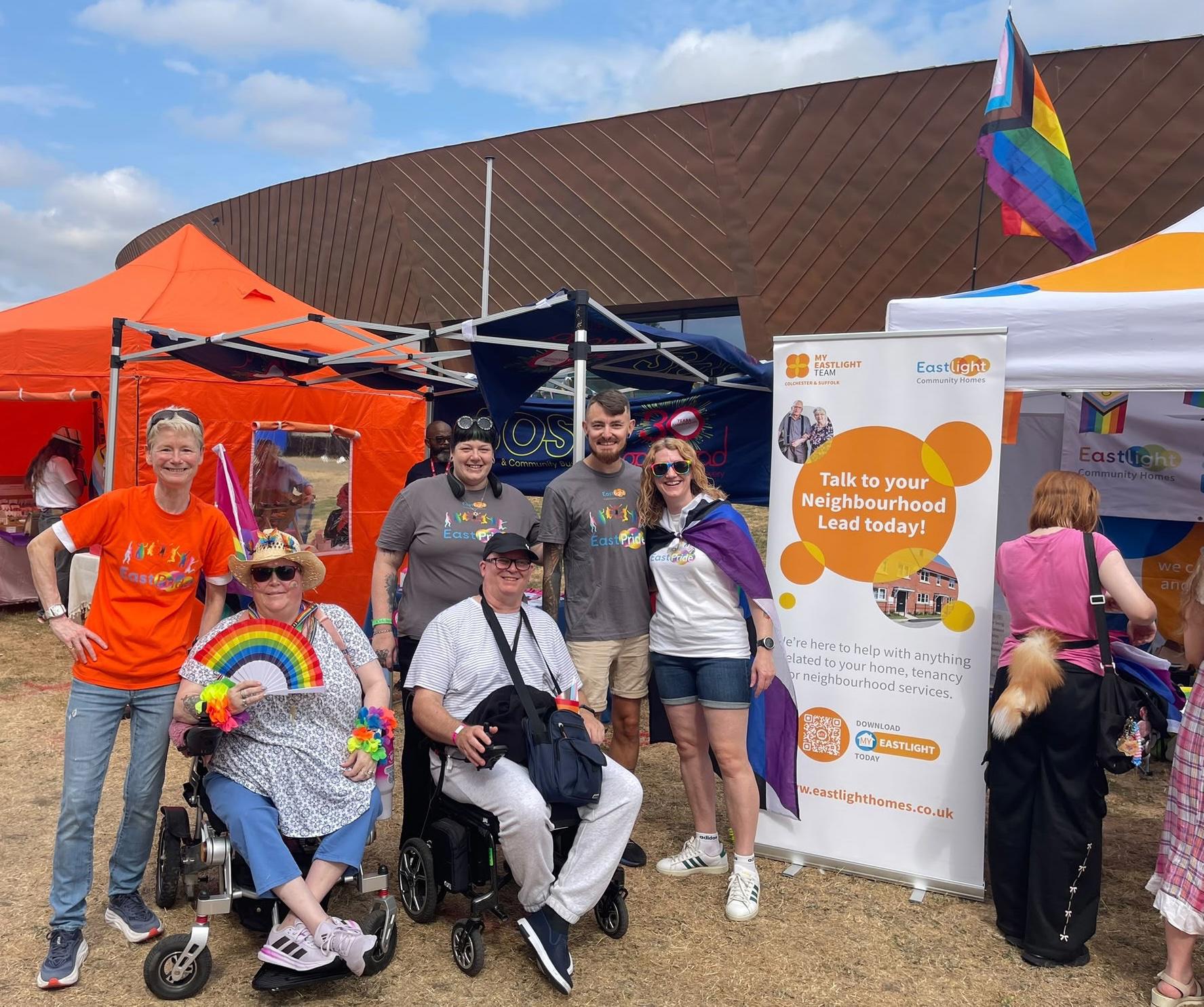 Eastlight colleagues and residents at a community Pride event, standing beside the Eastlight stall decorated with rainbow flags and information about local housing services.