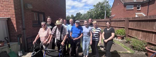 Eastlight residents and staff members pose for a group photo in a communal garden outside a housing scheme.