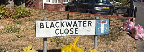 Several bags of litter and waste collected during an Eastlight community clean-up event, positioned next to the Blackwater Close street sign.