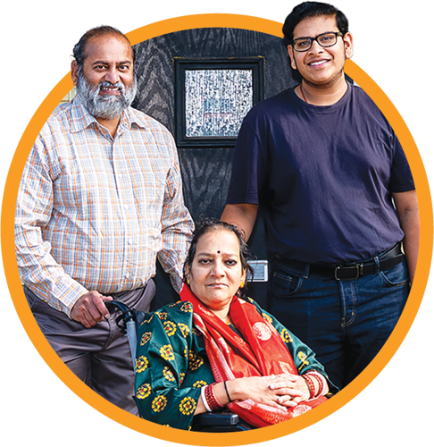 A group of three Eastlight residents posing on the front doorstep of their home for a photo. One person is seated in a wheelchair in front, and two people are standing behind, all framed within an orange circular border.