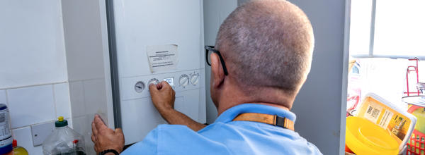  A member of Eastlight's Home Solutions Team carrying out a boiler check. He is photographed from behind and is wearing a blue top and an orange-coloured, Eastlight lanyard around his neck.