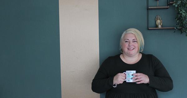 Gemma Griffin stood against a dark green wall in her new mental wellbeing hub. She is holding a Kinder Minds branded mug.
