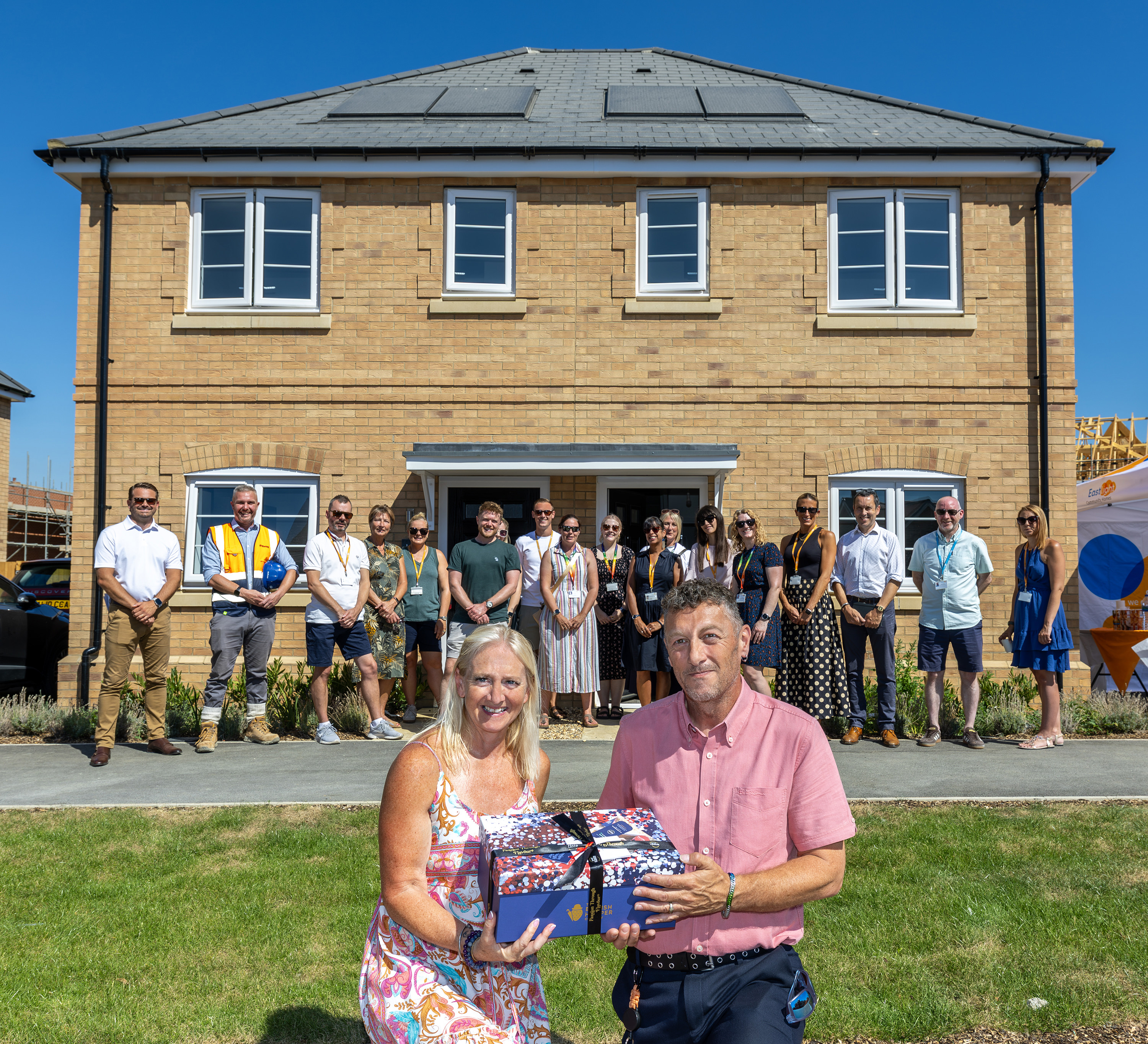 An Eastlight resident receives a gift during celebrations marking the delivery of Eastlight’s 2,000th new home, with Eastlight staff and partners gathered outside a newly built home in the background.