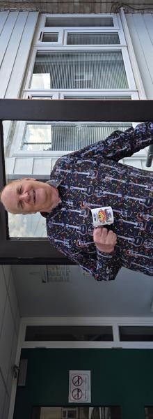 Dave Leslie is leaning on an open door with a mug in his other hand.