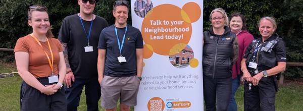 Members of Eastlight's Colchester & Suffolk Regional Team, together with a local police officer, standing in front of an Eastlight-branded banner. They are standing outside, with trees in the background. The Eastlight sign says “Talk to your Neighbourhood Lead today!”