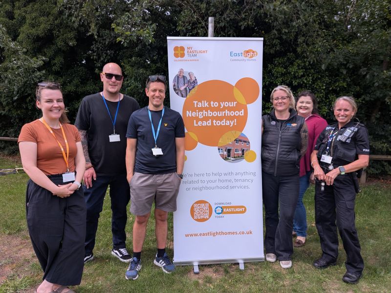 Members of Eastlight's Colchester & Suffolk Regional Team, together with a local police officer, standing in front of an Eastlight-branded banner. They are standing outside, with trees in the background. The Eastlight sign says “Talk to your Neighbourhood Lead today!”