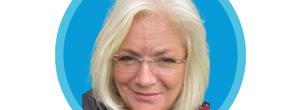 A blonde haired woman is smiling. She is wearing glasses.