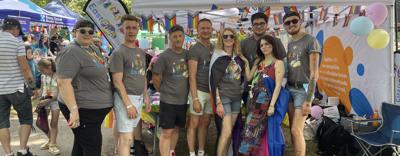 EastPride members standing in front of their stall at a Pride event, smiling at the camera. 