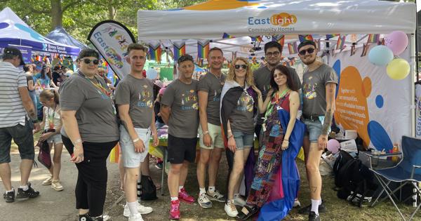 EastPride members standing in front of their stall at a Pride event, smiling at the camera. 