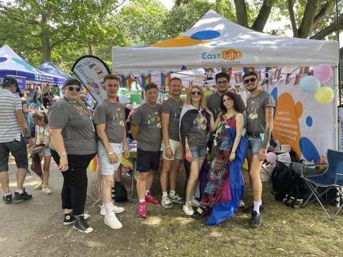 EastPride members standing in front of their stall at a Pride event, smiling at the camera.