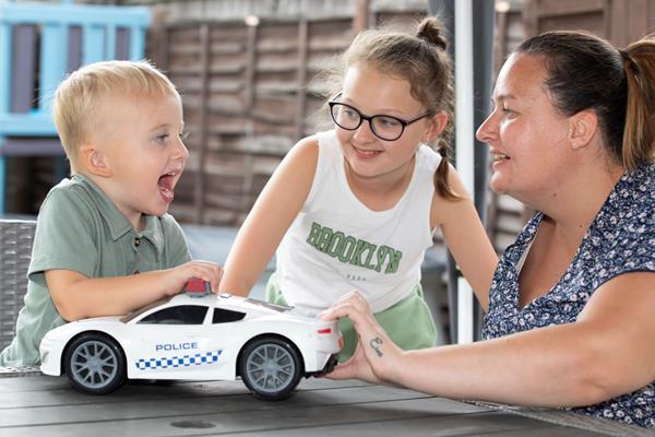 A family of three smiling and playing with a toy car