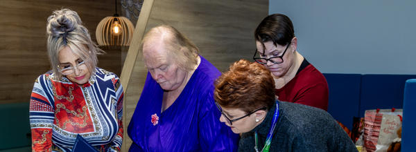 A group of four women are stood around a table looking at big pieces of paper which have been written on.