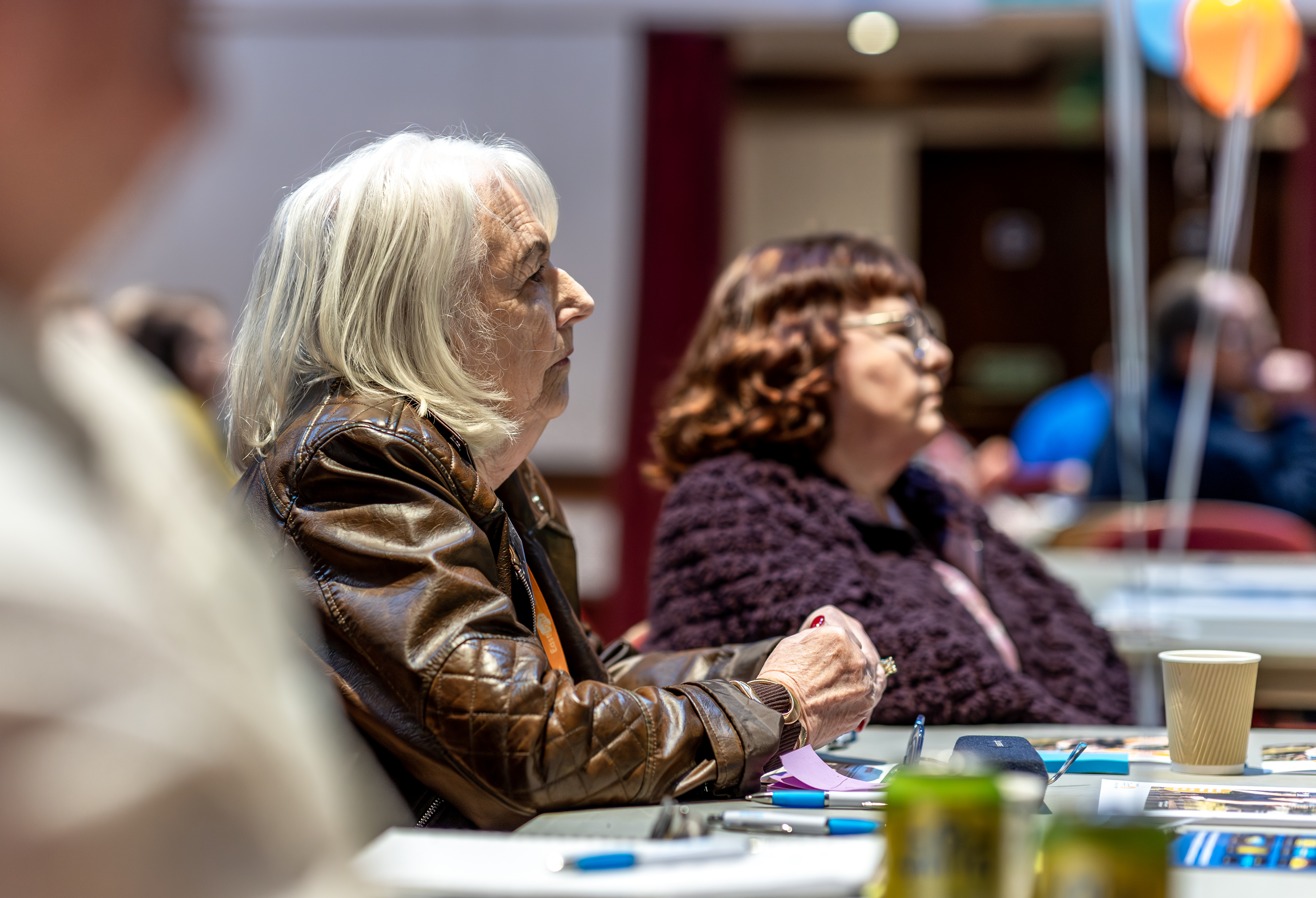 Two women are sat next to each other facing forwards. The image is taken from their right hand side to get a side shot of their faces.