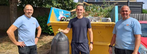 Members of Eastlight’s My Eastlight Team during a community clean-up event, with a skip containing collected waste and vegetation in the background.