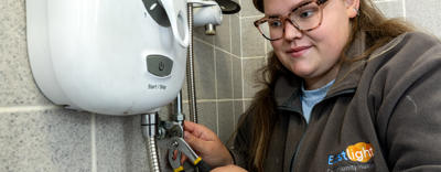 A young female plumber is working on a power shower unit.