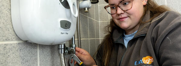 A young female plumber is working on a power shower unit.