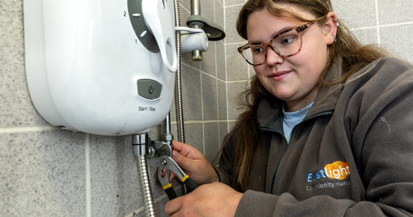 A young female plumber is working on a power shower unit.