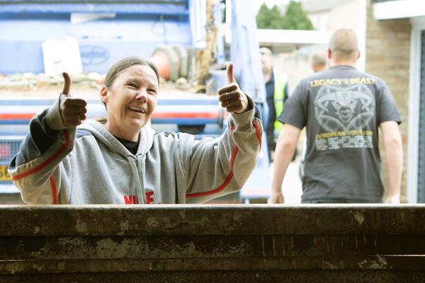 A woman in a grey hoodie is holding both thumbs up and smiling. This is after an estate clean up.